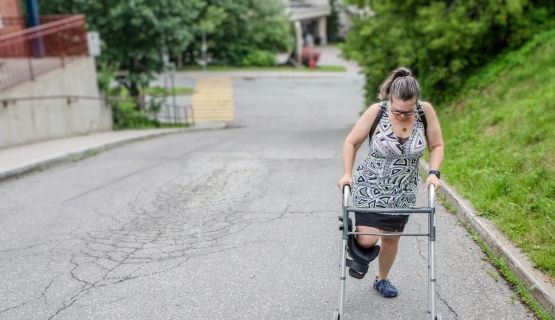 A woman with a leg cast and walker walks up a road.