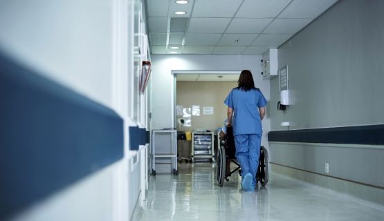 A long-term care worker pushes a resident in a wheelchair down the hall