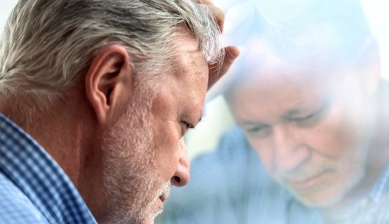 An grey-haired man leans his forehead against a window in deep contemplation