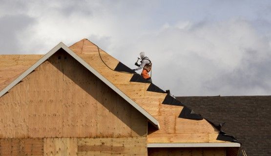 A lone roofing worker sits perched on top of a new being built