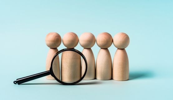 A magnifying glass is positioned in front of a row of five wooden figures