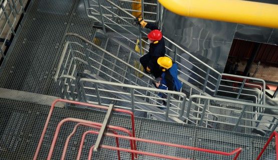 Overhead view of two people in safety helmets walking up the stairs in a plant
