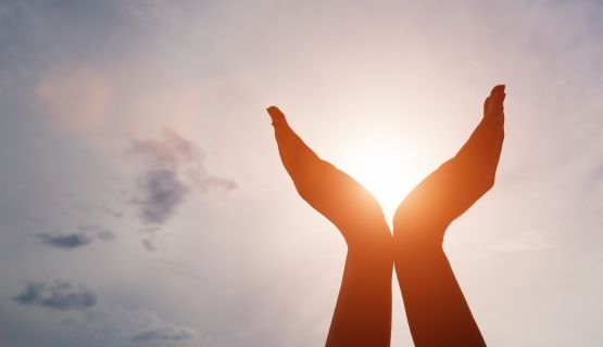 A silhouette of two palms held upward, cupping the sun