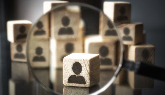 Silhouettes of people on cube wooden dice-size boxes, with magnifying glass focusing on one among them