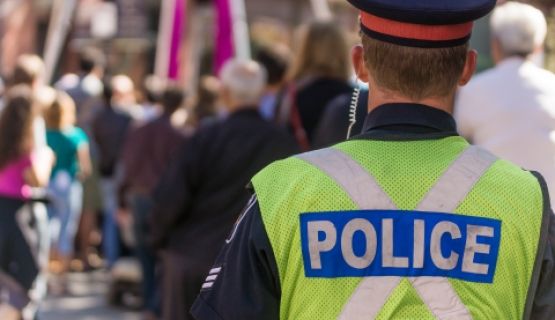 A police officer with their back turned faces a group of people walking around.