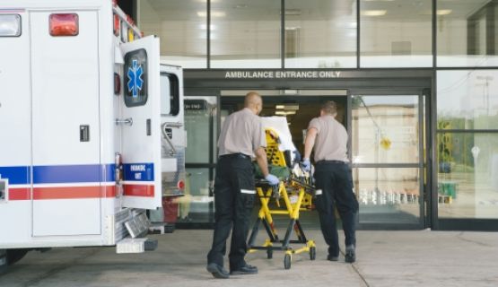 Paramedics wheel a stretcher out of a ambulance in front of a hospital.
