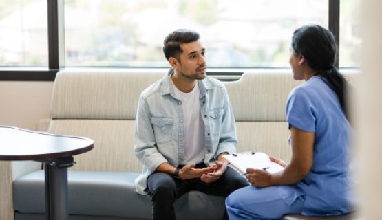 A man speaks with a female doctor in scrubs who holds a clipboard