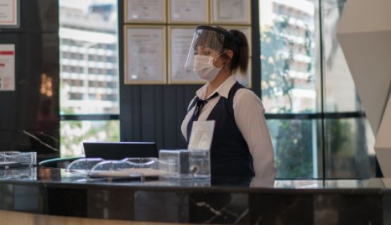 A masked young woman works at a hotel reception desk