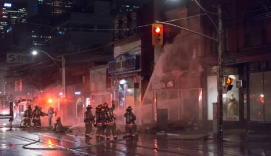 A group of firefighters aim a firehose at a building