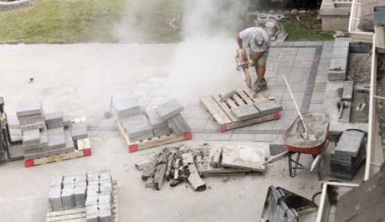 A worker bends over, cutting paving stones in a landscaping job