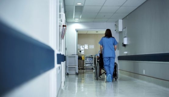 A long-term care worker pushes a resident in a wheelchair down the hall