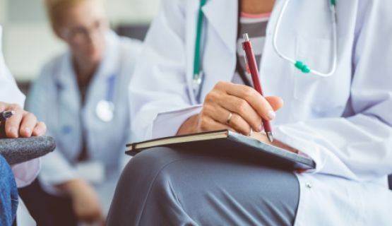 A group of physician's sitting in a room, prepared to take notes.
