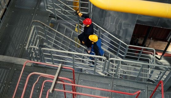 Overhead view of two people in safety helmets walking up the stairs in a plant